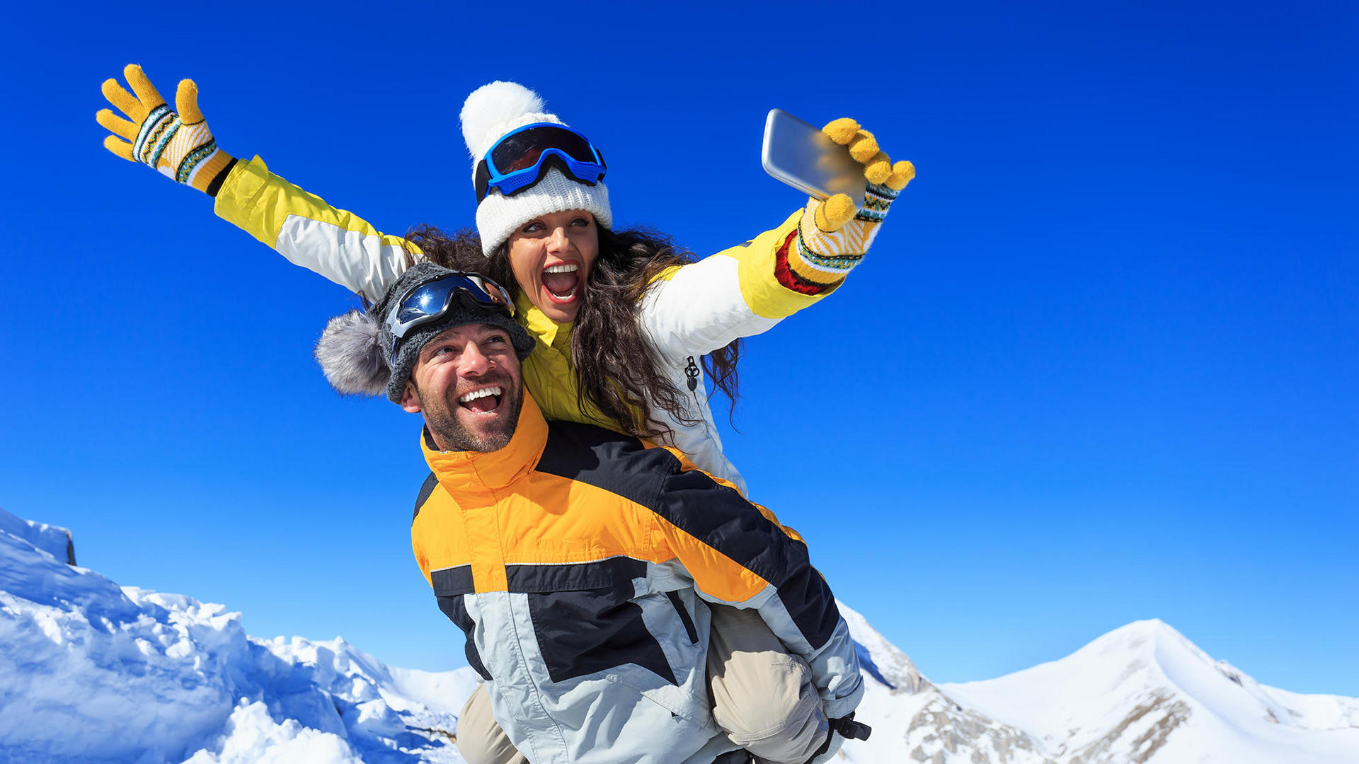 Man and woman taking selfie on top of snowy mountain