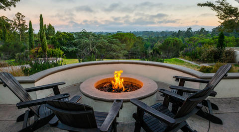 Outdoor seating area with fire pit overlooking green woodlands