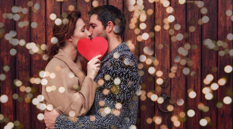 Man and woman kissing, holding love heart in front of faces