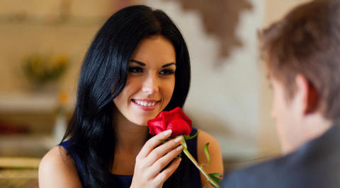 Woman smelling red rose while smiling at man